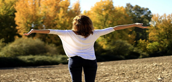 woman in field, arms outstretched looking at the fall colors, expressing gratitude